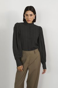 Blusa nera a righe con collare alto e maniche a sbuffo, abbinata a pantaloni marroni a righe sottili. Presenta una chiusura con bottoni e un tessuto testurizzato.