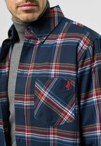 Marine geruite flanellen shirt met rode, witte en bruine lijnen. Voorzien van een button-down kraag en een borstzak met rode logo borduursel.