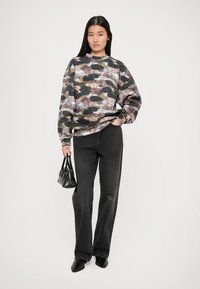 Sudadera de patrón camuflaje en tonos de verde, marrón y rosa, combinada con pantalones vaqueros de pierna ancha negros y un pequeño bolso negro.