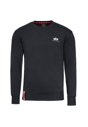 Czarna bluza crewneck z długimi rękawami, małe białe logo Alpha Industries na piersi oraz czerwona metka z tkaniny przy dolnym brzegu.
