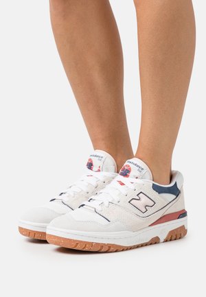 Białe i granatowe zamszowe sneakersy z różowym akcentem, z teksturowanym toe capem, białymi sznurówkami i gumową podeszwą. Widoczne logo "New Balance 550".