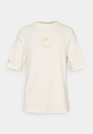 T-shirt à manches courtes de couleur crème en tissu texturé, avec un petit logo brodé sur la poitrine et une inscription sur la manche.