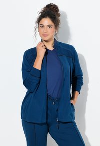 Chaqueta azul marino con cremallera, cuello alto y mangas largas, combinada con una camiseta a juego. Tela suave con una textura lisa y detalles mínimos.