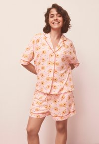 Set de pijama roz, cu mâneci scurte și pantaloni scurți, decorat cu un model de fructe galbene și inimi roșii, finisat cu bordură contrastantă.