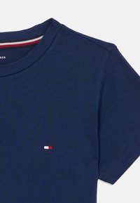 Μπλε μπλουζάκι από βαμβάκι σε ναυτικό μπλε χρώμα με στρογγυλή λαιμόκοψη, κοντά μανίκια και ένα μικρό κεντητό λογότυπο σε κόκκινο, άσπρο και μπλε στο στήθος.