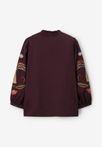 Bordeauxrode blouse met geborduurde bloem- en diermotieven op de lange mouwen, geplooide manchetten en een gerimpelde halslijn.