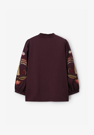 Blouse bordeaux avec des motifs brodés de fleurs et d'animaux sur les manches longues, des poignets froncés et un col à volants.