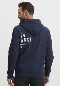 Sudadera azul marino hecha de mezcla de algodón, con cordón, bolsillo frontal y texto y gráficos impresos en blanco en la parte posterior.