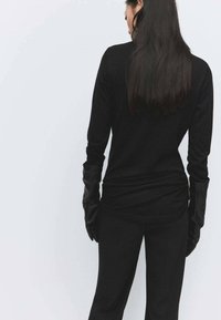 Top negro de manga larga combinado con pantalones ajustados negros, usado con guantes de cuero negros, destacando una silueta elegante y una textura suave.