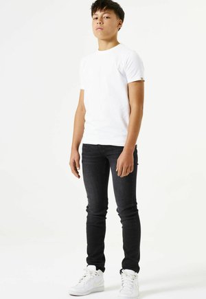 Weißes T-Shirt mit kurzen Ärmeln, dunkle Skinny-Jeans und weiße Sneaker. Einfaches Design und figurbetonte Form. Keine sichtbaren Muster oder Akzente.