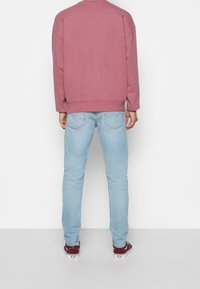 Sudadera rosa de cuello redondo con hombros caídos, combinada con vaqueros azul claro. Lleva zapatillas rojas y blancas. Un conjunto simple y casual.