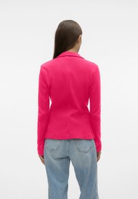 Blazer rosa aderente con design a un solo petto, revers a punta e polsini con bottoni, abbinato a jeans azzurri chiari. Texture liscia.