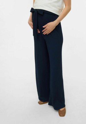 Pantaloni a gamba larga blu navy realizzati in tessuto strutturato, con un fiocco in vita. Abbinati a scarpe slip-on color cammello.