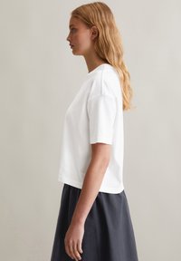 T-shirt blanc à manches courtes avec un fit décontracté et une texture côtelée, associé à une jupe gris foncé. Lignes épurées et design minimaliste.