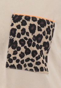 Un bolsillo de estampado de leopardo en una tela beige, con manchas negras y marrones y un acento naranja en el borde. Textura suave.