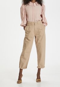 Helle rosa plissierte Bluse mit Kragen und Puffärmeln, kombiniert mit hochgeschnittenen beige Hosen mit umgeschlagenen Säumen und braunen Sandalen.