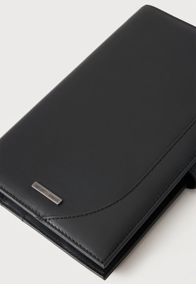 Portefeuille en cuir noir avec finition lisse et une petite plaque métallique rectangulaire avec le logo Emporio Armani dans le coin.