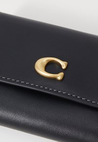 Black leather wallet featuring a prominent gold crescent moon clasp, with white stitching along the edges for added detail.