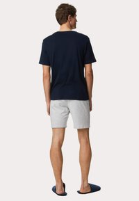 Camiseta de algodón navy, pantalones cortos grises y zapatillas oscuras llevadas por una persona de espaldas. La camiseta tiene cuello redondo y un ajuste casual.