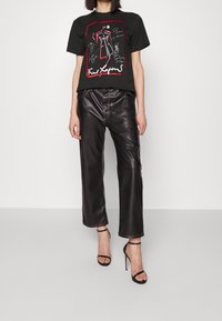 Camiseta negra con estampado de ilustración de moda en rojo y blanco, combinada con pantalones de imitación cuero negro brillantes de pierna ancha y tacones negros con tiras.