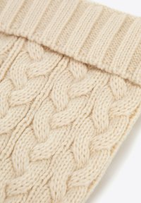 Kremowa dzianina w warkocze, prezentująca teksturowany wzór z skręconymi linami. Posiada ściągacz na górnym brzegu, grubą przędzę i miękkie wykończenie.