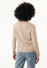 Beige pletený svetr s dlouhými rukávy a kulatým výstřihem, s žebrovanými manžetami a spodním lemem. V kombinaci se světle modrými džíny.