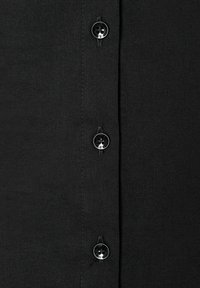 Schwarzes Stoffhemd mit einer Reihe glänzender schwarzer Knöpfe mit Totenkopfdesigns, glatter Textur und kontrastierenden Nähdetails.