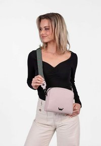 Světle růžová crossbody taška s texturovaným designem, nastavitelným vzorovaným poutkem, detaily loga a zipovým uzávěrem. Kompaktní a obdélníkový tvar.
