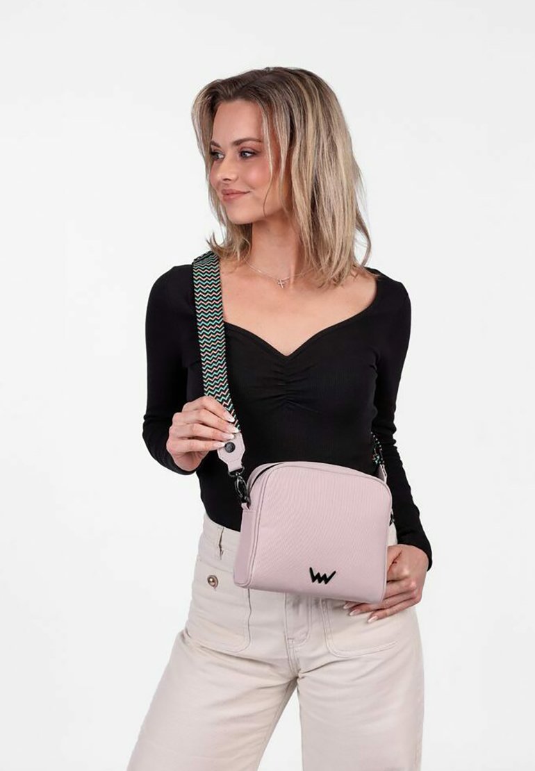 Světle růžová crossbody taška s texturovaným designem, nastavitelným vzorovaným poutkem, detaily loga a zipovým uzávěrem. Kompaktní a obdélníkový tvar.