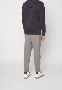 Ciemnoszara bluza z kapturem o luźnym fasonie, zestawiona z jasnoszarymi spodniami dresowymi i białymi sneakersami z niebieskim logo Nike na pięcie.