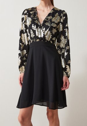 Czarna sukienka z długimi rękawami, złotym kwiatowym wzorem na górze, dopasowaną talią oraz rozkloszowaną spódnicą kończącą się powyżej kolan.