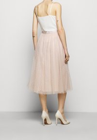 Une jupe en tulle rose à pois, longueur genoux, associée à un top blanc à fines bretelles et des talons nude. Dotée d'une ceinture ajustée.