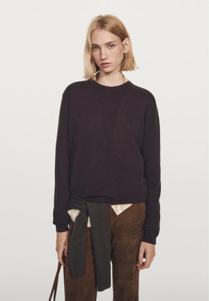 Mørk lilla sweater med lange ærmer og rund halsudskæring, parret med en lys skjorte og brune bukser. Sweateren har en blød tekstur.