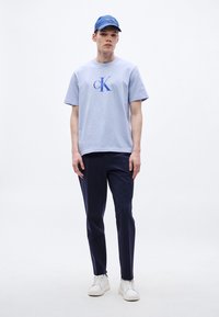 Jasnoniebieska bawełniana koszulka z ciemnoniebieskim logo "CK", zestawiona z granatowymi spodniami i białymi trampkami. Czapka na co dzień w kolorze pasującym do koszulki.