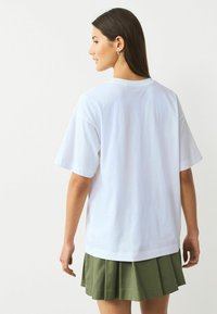 Tricou alb din bumbac cu mâneci scurte, croială lejeră și decolteu rotund, asortat cu o fustă plisată verde măsliniu.