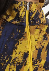 Fleece-Halbzip-Pullover in blauem und gelbem abstraktem Muster. Mit hohem Kragen und einem Reißverschluss mit einer metallischen Ziehschlaufe.