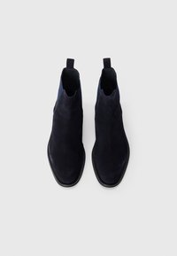 Ein Paar schwarze Wildleder Chelsea-Stiefel mit Zuglaschen, abgerundeten Zehen und elastischen Seitenpaneelen auf einem schlichten weißen Hintergrund.