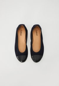 Ballerines en daim navy avec un bout en cuir noir. Elles présentent une texture lisse et une semelle intérieure perforée, conçues pour le confort.