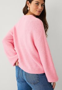 Maglione rosa soffice con vestibilità rilassata e oversize, spalle scese e orlo a coste, abbinato a jeans di denim blu. Texture morbida.