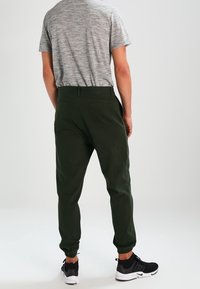 Ciemnozielone dresy z elastycznymi mankietami, kieszeniami i luźnym krojem, połączone z szarym t-shirtem z krótkim rękawem i czarnymi butami sportowymi.