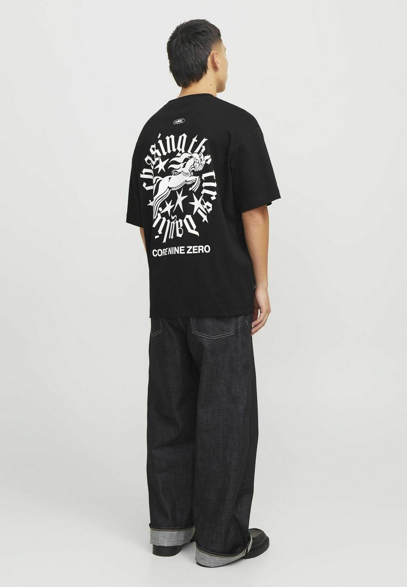 Sort oversized t-shirt med hvid grafisk print, der viser en figur, stjerner og tekst på ryggen. Kombineret med mørk denimjeans.