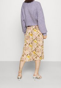 Lila fluffig tröja med vida ärmar, matchad med en blomstrande midi kjol med gula och vita blommor på en rosa bakgrund. Vita klacksandaler.