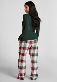 Groene lange mouwen top gecombineerd met rood, wit en zwart geruit pyjamabroek. Zacht stof, relaxte pasvorm, met een geruit patroon op de broek.