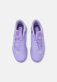 Lilla sportssko med en glat, tekstureret overflade, der har snørebånd, en pull-tab og et kontrasterende neongult logo.