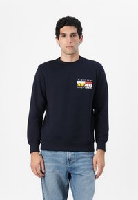 Marineblå bomullssweatshirt med ribbestrikkede mansjetter og krage. Har en flerfarget "Tommy Hilfiger"-logo på brystet. Klassisk passform.