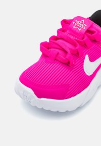 Scarpa atletica di un vivace colore rosa con una texture in tessuto a righe, dettagli bianchi e chiusura con lacci. Presenta una linguetta imbottita e un logo del marchio sul tallone.