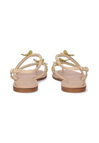 Sandalias planas con una base beige, adornadas con acentos dorados y un diseño de tiras entrecruzadas. Textura suave y taco mínimo.