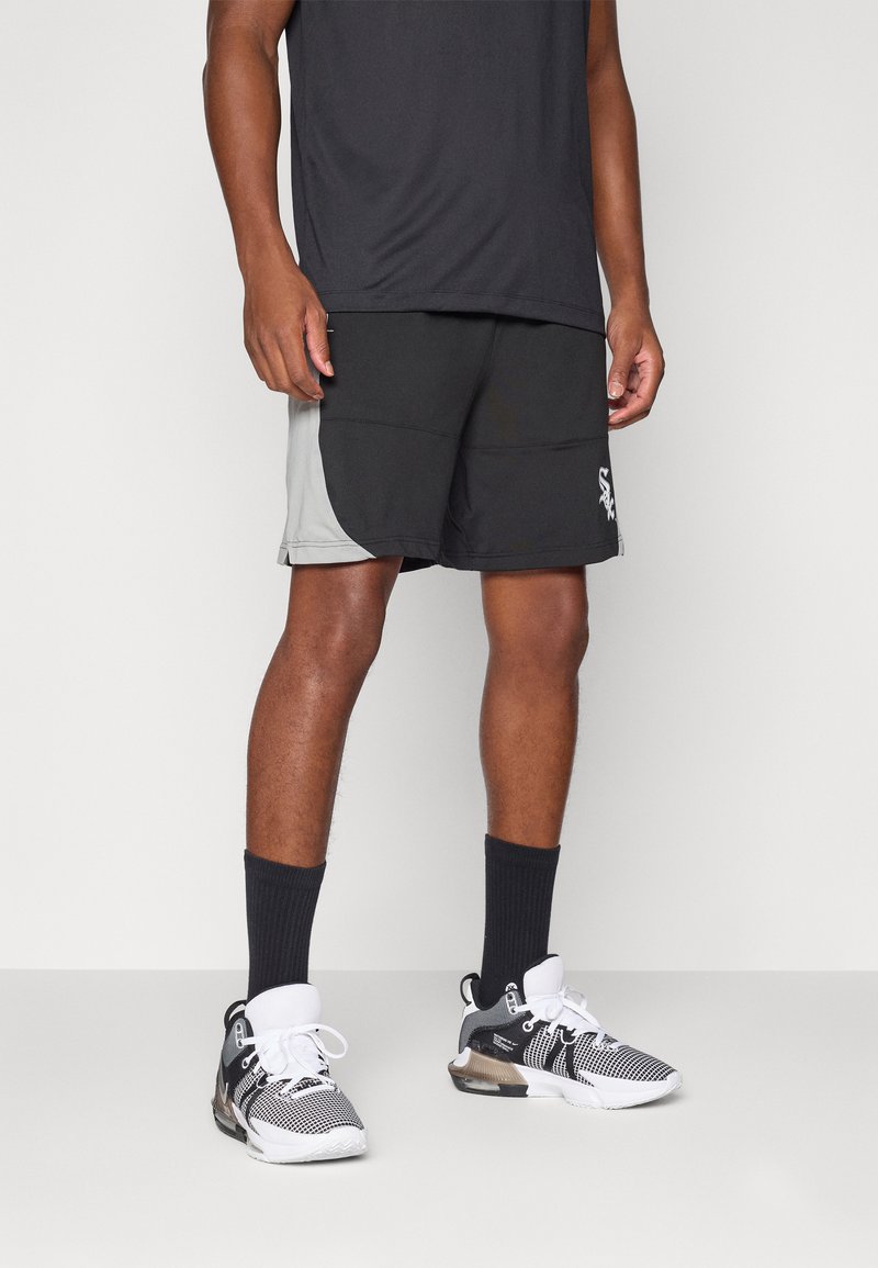 Svart og grå idrettsshorts med mesh-struktur, sidelommer og en logo på underbenet, kombinert med svarte sokker og sporty sko.