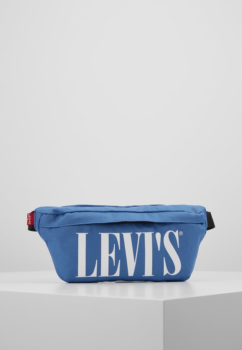 Sac banane bleu Levi's avec texte de logo blanc, sangle noire réglable et étiquette rouge Levi's sur le côté, posé sur une surface blanche.