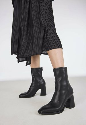 Svarta läderankelboots med fyrkantig tå och tjock klack, med en slät yta och en sidogångjärn för stängning.